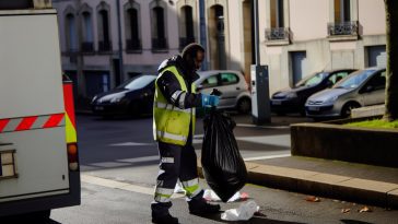 Un éboueur en tenue de travail, ramassant des sacs poubelles dans la rue.