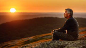 Une personne seule, assise au sommet d'une colline, regardant l'horizon pendant le coucher du soleil.