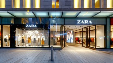 Une vue extérieure d'un magasin Zara avec sa vitrine bien éclairée et ses vêtements exposés.