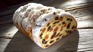 Un Stollen d'Alsace traditionnel, généreusement saupoudré de sucre glace, posé sur une table en bois rustique.