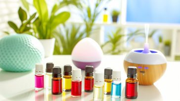 Un assortiment d'huiles essentielles de différentes couleurs dans de petits flacons avec un diffuseur d'huiles essentielles en arrière-plan.
