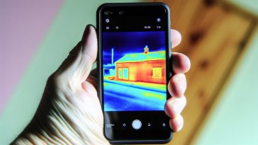 Une main tenant un smartphone, affichant sur son écran une image thermique d'une maison.