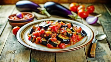 Un plat de caponata d'hiver aux aubergines et tomates, coloré et appétissant, servi dans une assiette rustique sur une table en bois.