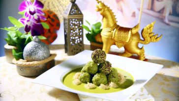Un plat de curry vert thaï, garni de boulettes de quinoa, présenté de manière appétissante sur une table avec des éléments de décoration exotiques.