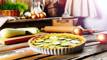Une quiche courgettes, oignons et chèvre fraîchement préparée et appétissante sur une table rustique.